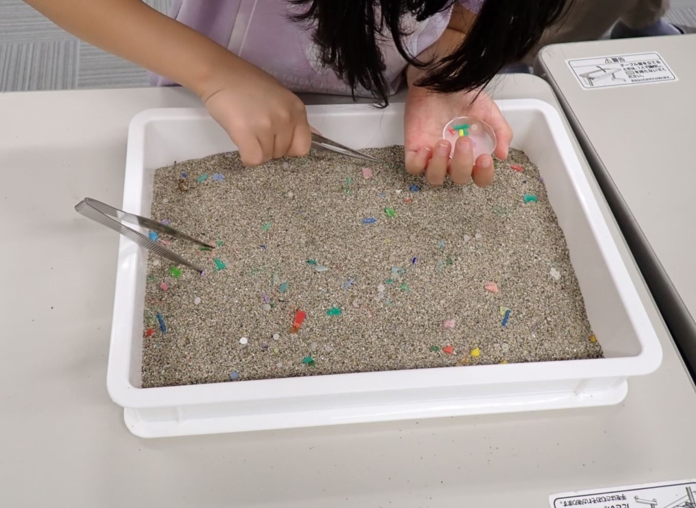 砂の中からプラスチックを拾う